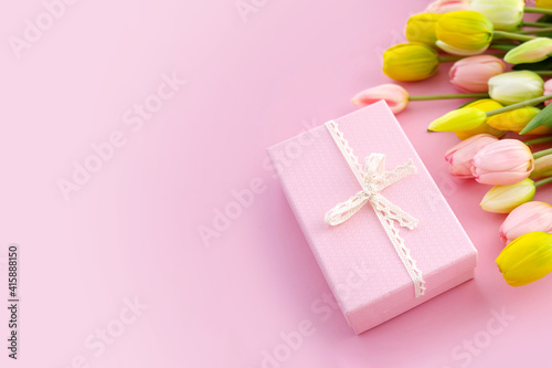 Bouquet of colorful tulips and gift box isolated on pink background. Spring flowers. Greeting card for Birthday, Woman, Mother's Day, Valentine's day. Flat lay. Copy space.
