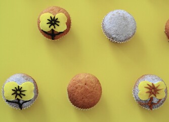 Rows of muffins decorated with powdered sugar and yellow flower shaped icing on a yellow background