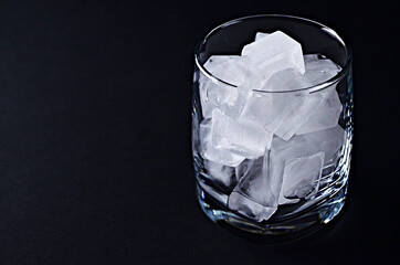 A glass full of ice cubes stands on a black table close up with a copy space. High quality photo