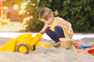 Little girl having lots of fun with her toys playing in the sandbox