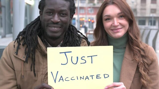 Young multiethnic couple holding banner just vaccinated, they smiling in camera and each other, concept of encouraging to vaccinate against coronavirus reaching the herd immunity achievement