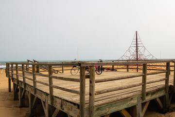 Wooden platform with some bicycles, on a beach with cloudy skies on a cold winter day.