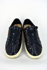 Stylish bright black lacquer shoes located on a white background. Moccasins made of genuine leather with bullshit and black wide laces. Women's sneakers on a white tast sole. 