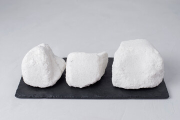 Large crystals of sodium chloride- food salt on a black stone board. Food flavor enhancer. Organic NaCl natural minerals on light background. 