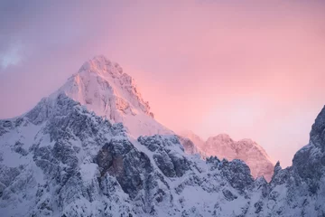 Fotobehang Lichtroze Beautiful close up shot of a pink glowing Mountain top in the Alps at sunset while wind is blowing snow off the Mountain. Power of natural elements in an alpine environment  © RoMaLi