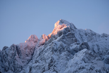 Beautiful close up shot of a pink glowing Mountain top in the Alps at sunset while wind is blowing snow off the Mountain. Power of natural elements in an alpine environment