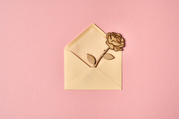 Top view of a wooden rose in an envelope on pink paper background