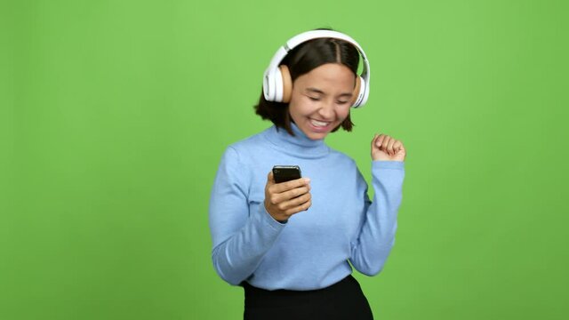 Young brunette woman  listening music with a mobile and dancing over isolated background. green screen chroma key