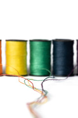 Tread unwinding from spools, yellow, green and blue spools on white in background 