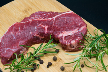 Beef steak, view of fresh beef on a wooden board with rosemary, black pepper, lavatory leaf