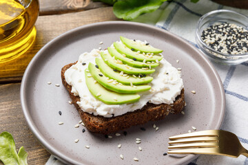 Rye bread toast with avocado and cream cheese on wooden table background. Close up