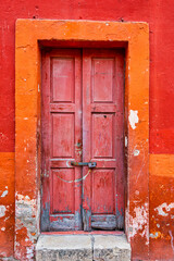 An old faded red door with an orange frame and a red wall