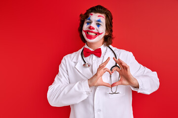 friendly caucasian doctor in the form of clown showing heart at camera, love and healthcare concept