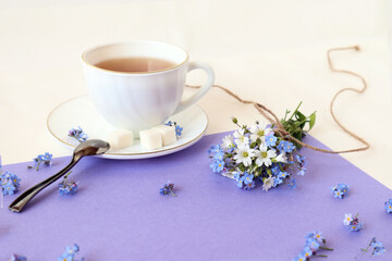 Bouquet of wild flowers on the background of a cup of tea on a white-purple background, side view