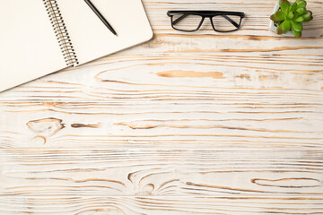 Photo above of notepad plant pen and glasses on the wood table