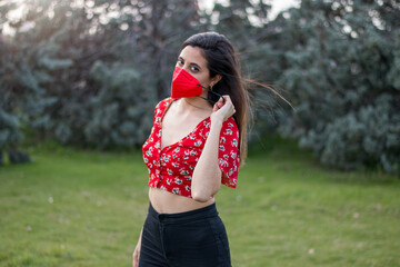 Hispanic girl taking off face mask in nature. Wearing colorful clothes.