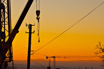 Silhouette of a crane on a background of sunset. Ropes and hooks on an orange background.