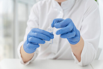 doctors hands in blue protective gloves hold transparent vial with liquid medicine and is going to shake it off. Preparation for injection. Vaccination concept