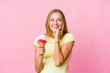 Young russian woman eating an ice cream isolated keeps hands under chin, is looking happily aside.