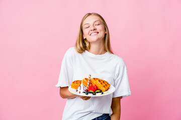Young russian woman eating a waffle isolated laughs and closes eyes, feels relaxed and happy.