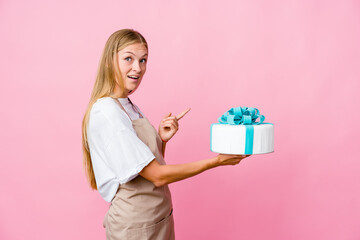 Young russian baker woman holding a delicious cake excited holding a copy space on palm.