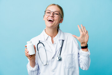 Young russian doctor woman holding pills bottle on blue showing number ten with hands.