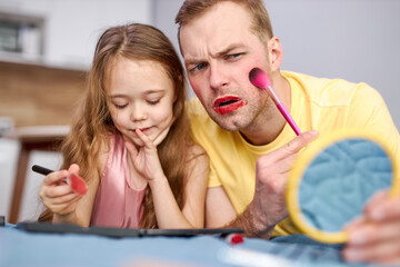 daddy and daughter doing makeup together, little daughter using decorative cosmetics, having fun playing enjoying time with parent at home at weekends. man looking at mirror with confusion