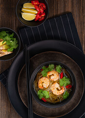 thai soup in a black bowl on wooden table.