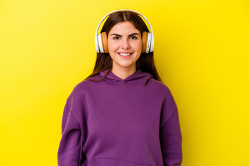 Young caucasian woman listening to music with headphones isolated on pink background happy, smiling and cheerful.