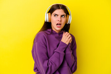Young caucasian woman listening to music with headphones isolated on pink background scared and afraid.
