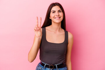 Young caucasian woman isolated on pink background showing victory sign and smiling broadly.