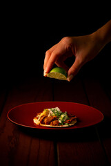 Tasty taco al pastor on red plate squeezing lemon
