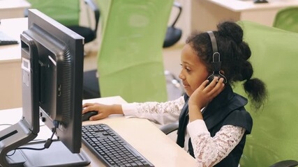 In school schoolgirl study, focused little African girl wear headphones and listen to a lesson using computer. - Powered by Adobe