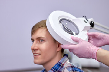 female trichologist using dermatoscope while examining male head and hair. in bright cosmetology...