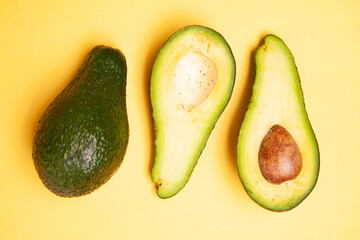 Halved and whole avocados on yellow table