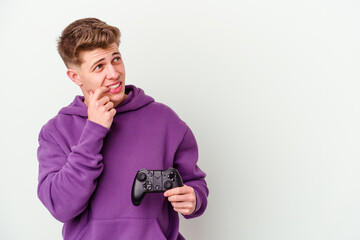 Young caucasian man holding a gamepad isolated on white background relaxed thinking about something looking at a copy space.