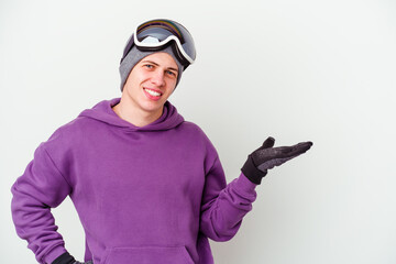 Young man holding a snowboard board isolated on white background showing a copy space on a palm and holding another hand on waist.
