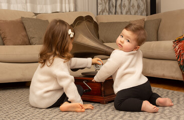 Adorable brother and sister playing on the floor with gramophone. Sibling play together at home. Toddler girl and baby boy in the living room. Hobby for children. Kids and music. Retro record music.