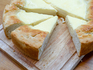Close-up of triangular slices of sour cream pie - a national Tatar dish. A huge homemade cheesecake with toasted edges and tender filling on a wooden table.