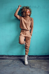 Young smiling fashionable woman with curly hair leaning against the wall.