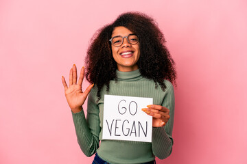 Young african american curly woman holding a go vegan placard smiling cheerful showing number five with fingers.