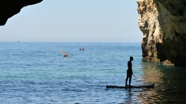Silhouette of man on paddle board in the emerald sea of Algarve caves