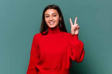 Young Indian woman isolated on blue background showing victory sign and smiling broadly.