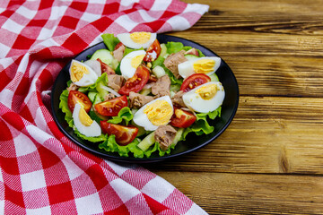 Tasty tuna salad with eggs, lettuce and fresh vegetables on wooden table
