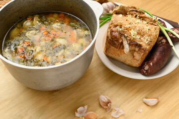 baked meat, soup and blood sausage on a plate, green onion and garlic on wooden background, home...