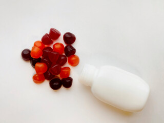 Group of red, orange and purple multivitamin gummies with the bottle isolated on white background. Healthy lifestyle concept..