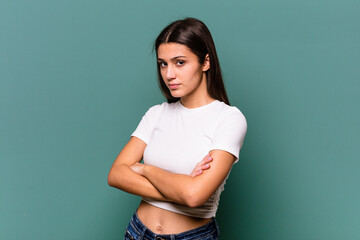 Young Indian woman isolated on blue background frowning face in displeasure, keeps arms folded.