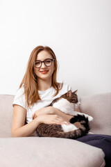 Beautiful woman with cute cat at home. Beautiful middle-aged woman at home on the couch in the interior. Playing with cat at home. Playing with pet. Young woman sitting on couch and hugging pet.