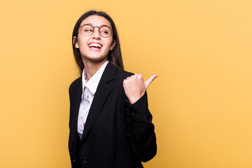 Young Indian business woman isolated on yellow background points with thumb finger away, laughing and carefree.