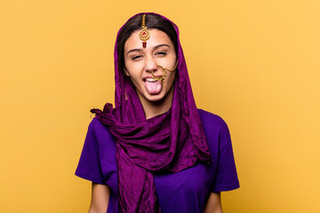 Young Indian woman wearing a traditional sari clothes isolated on yellow background funny and friendly sticking out tongue.